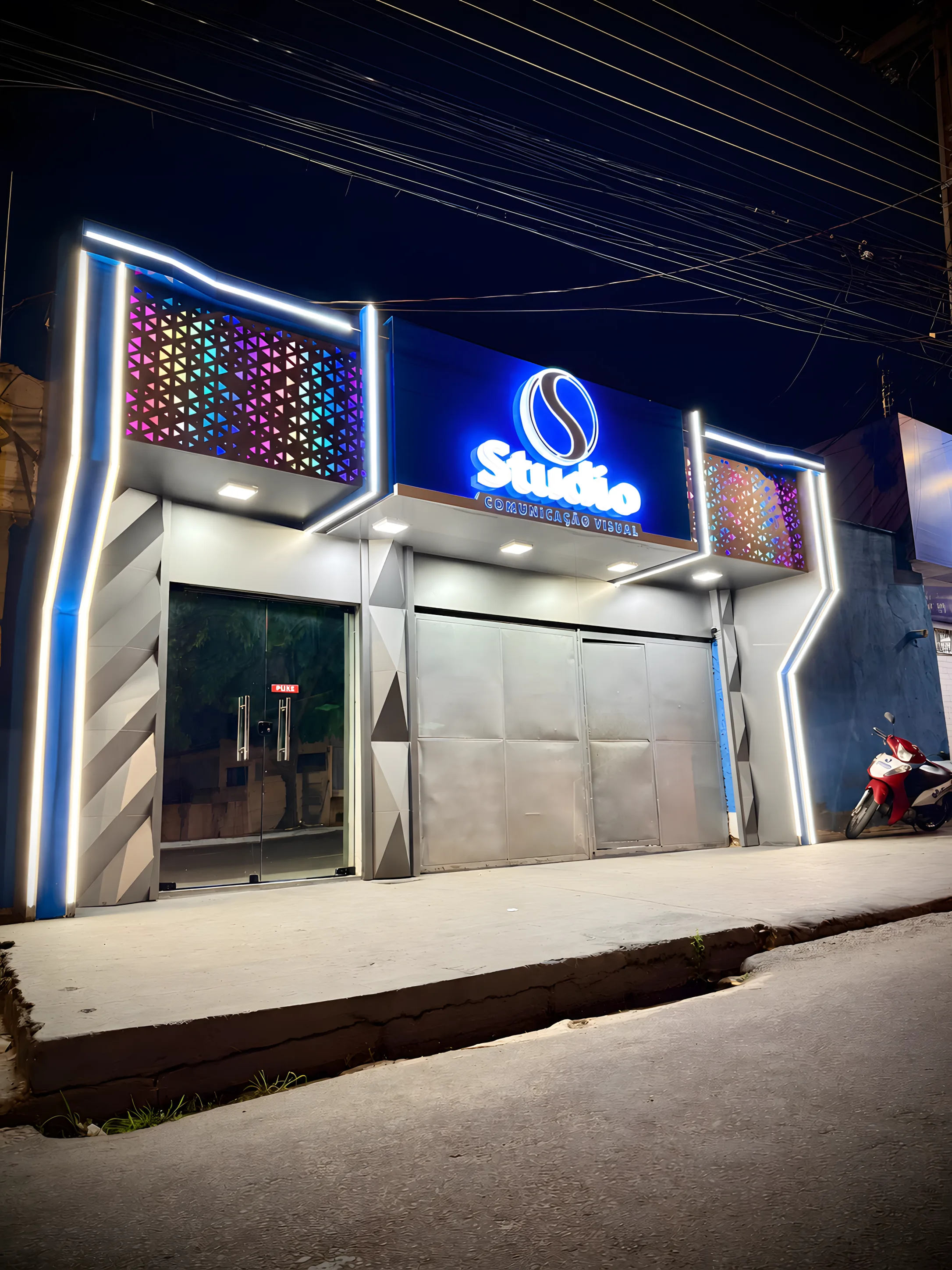 Fachada da Studio Comunicação Visual à noite, com letreiro e contornos iluminados